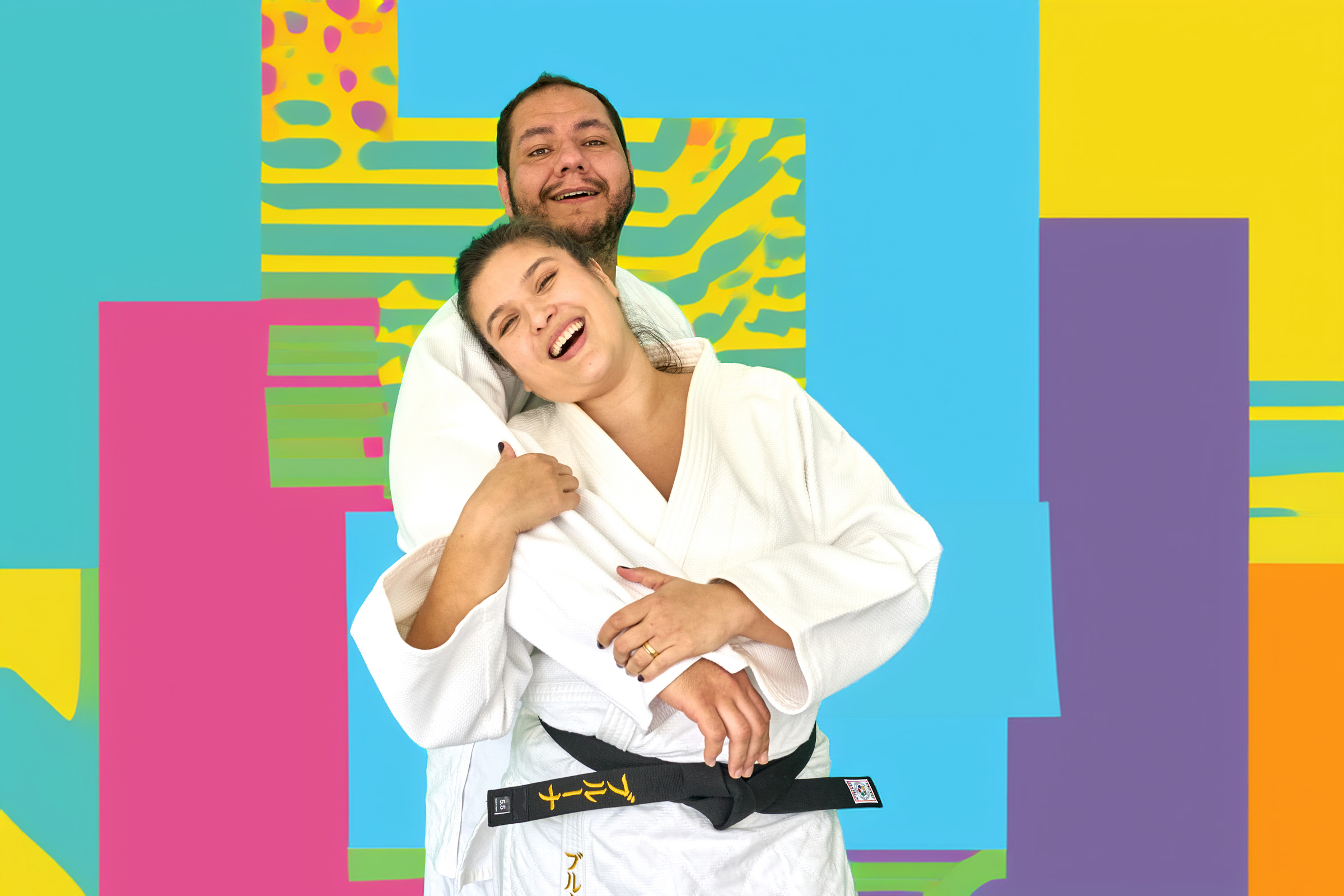 Rafael Silva e Bruna Luísa de kimono, rindo, sobre fundo colorido